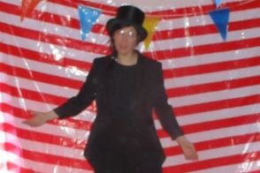 Eine Frau steht als Zirkusdirektorin vor einem gestreiften Vorhang